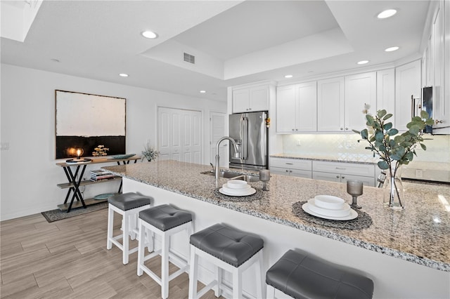 kitchen featuring light stone counters, high end fridge, white cabinetry, and a tray ceiling