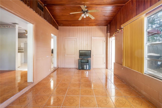 unfurnished living room featuring wood walls, light tile patterned flooring, wooden ceiling, and ceiling fan