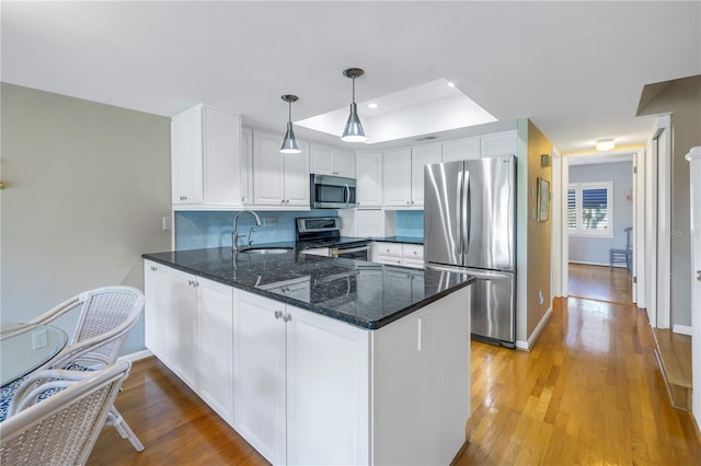 kitchen featuring pendant lighting, kitchen peninsula, white cabinetry, light hardwood / wood-style flooring, and stainless steel appliances