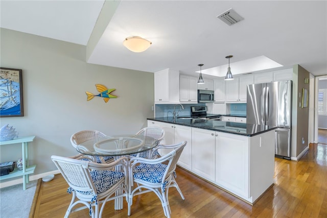 kitchen with white cabinetry, stainless steel appliances, decorative light fixtures, light wood-type flooring, and sink