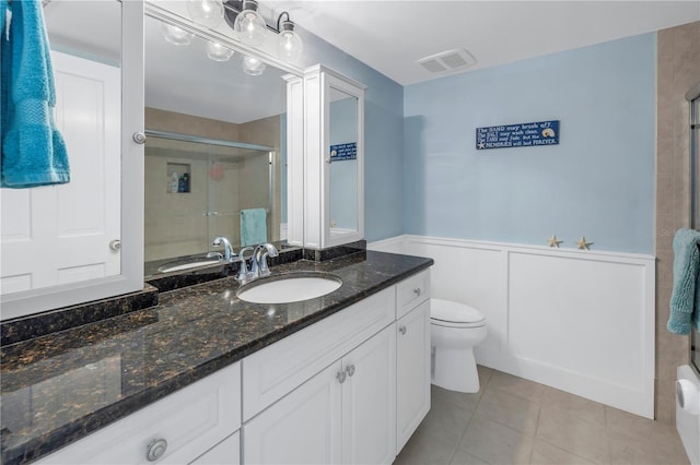 bathroom featuring toilet, vanity, tile patterned floors, and a shower with door