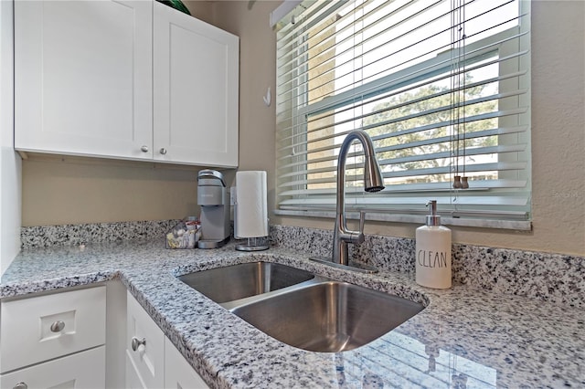 kitchen with white cabinets, sink, and light stone countertops