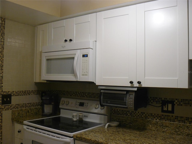 kitchen featuring tasteful backsplash, dark stone countertops, white cabinets, and white appliances