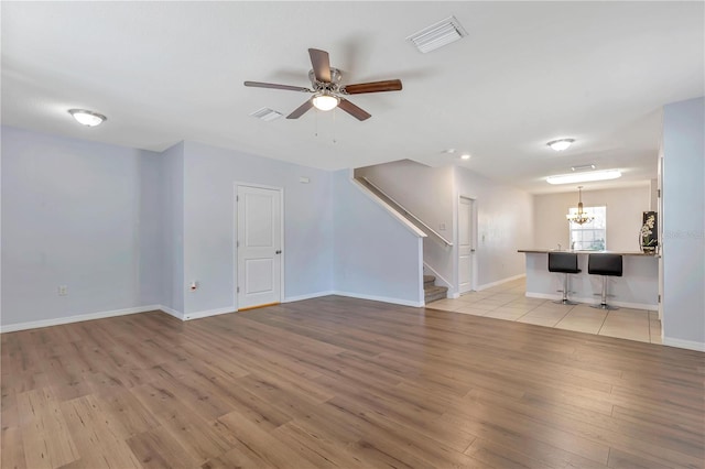 unfurnished living room with ceiling fan with notable chandelier and light hardwood / wood-style floors