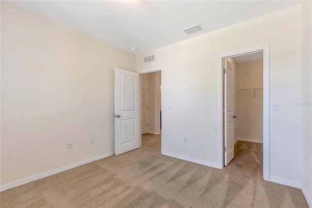 unfurnished bedroom with a closet, a spacious closet, and light carpet