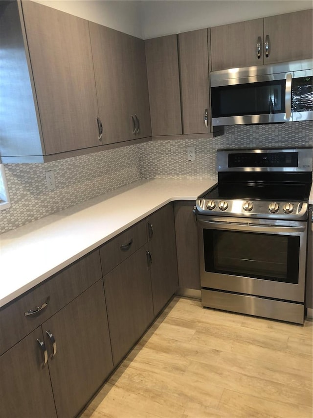 kitchen featuring dark brown cabinets, backsplash, appliances with stainless steel finishes, and light wood finished floors