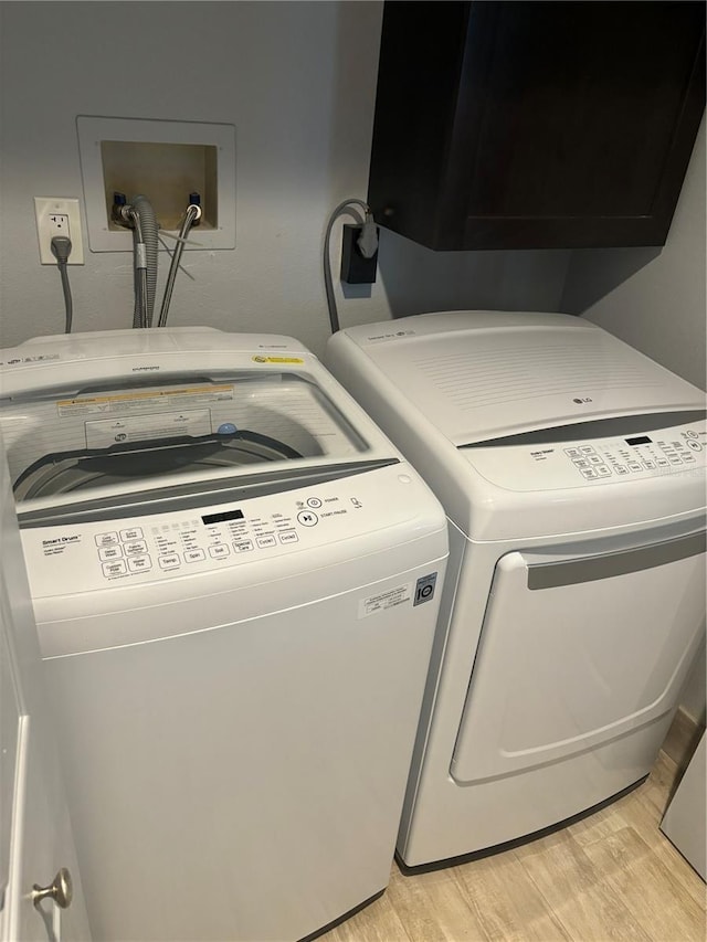 laundry room with cabinet space, light wood-style floors, and separate washer and dryer