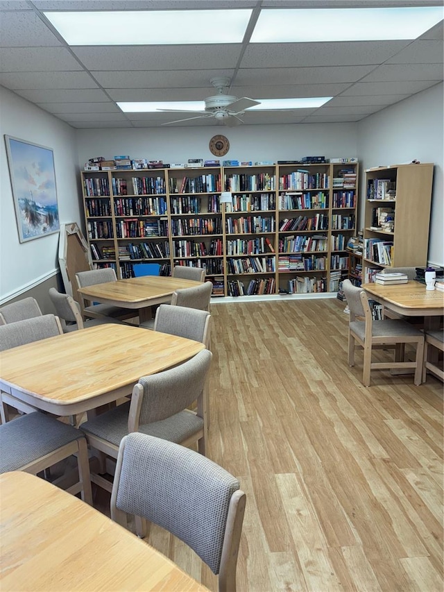 office area featuring ceiling fan, a drop ceiling, wood finished floors, and bookshelves