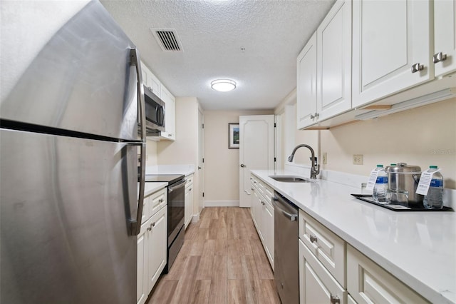 kitchen with stainless steel appliances, light hardwood / wood-style floors, a textured ceiling, white cabinets, and sink