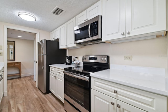 kitchen featuring light stone counters, a textured ceiling, white cabinets, light wood-type flooring, and stainless steel appliances