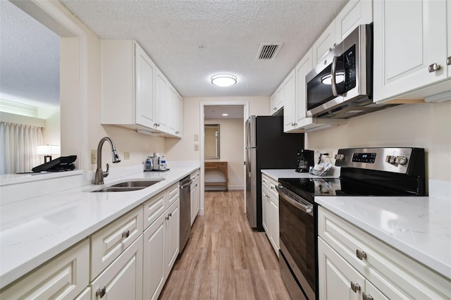 kitchen featuring a textured ceiling, white cabinets, sink, stainless steel appliances, and light hardwood / wood-style flooring