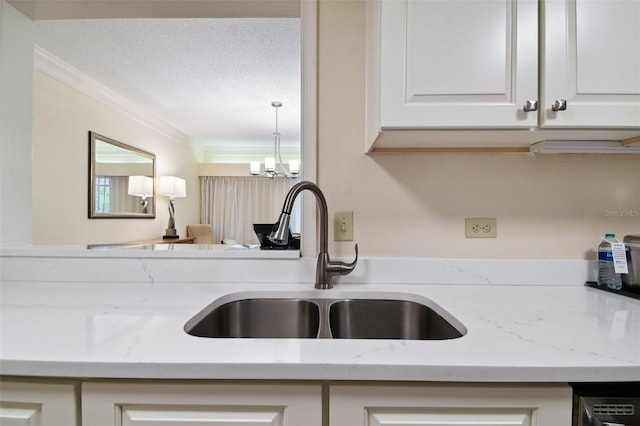 kitchen with crown molding, a textured ceiling, white cabinets, sink, and a notable chandelier