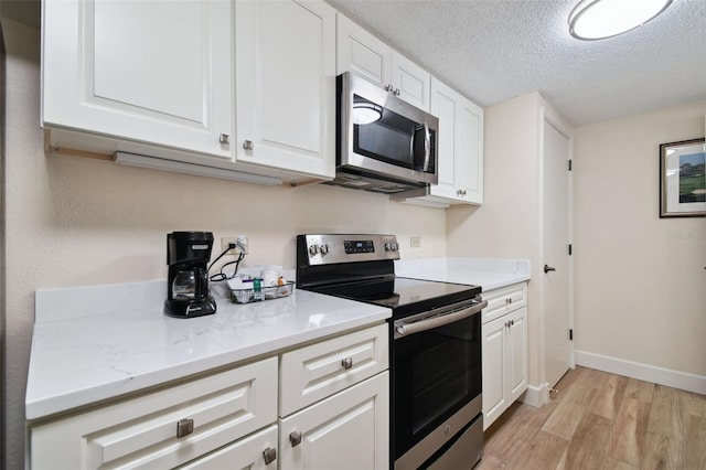 kitchen featuring white cabinetry, appliances with stainless steel finishes, light stone counters, light hardwood / wood-style floors, and a textured ceiling