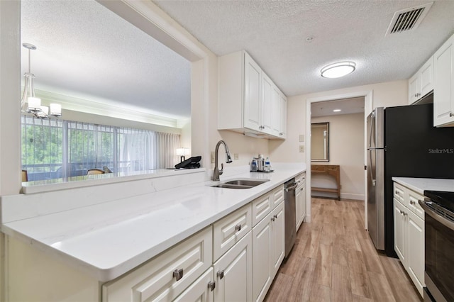 kitchen featuring white cabinets, sink, light wood-type flooring, stainless steel appliances, and pendant lighting