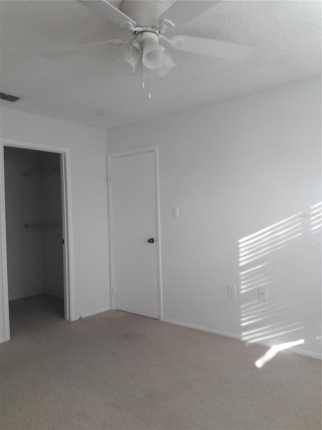 unfurnished bedroom featuring a walk in closet, carpet, a closet, and ceiling fan