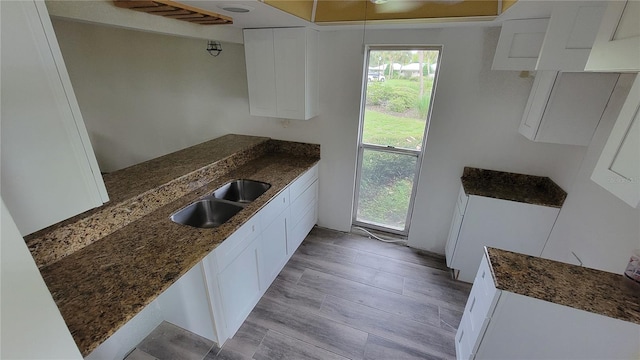 kitchen featuring sink, light hardwood / wood-style flooring, white cabinets, and dark stone counters