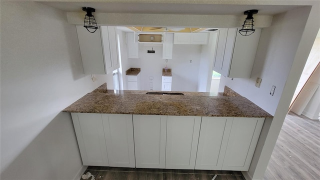 kitchen featuring hanging light fixtures, dark stone counters, wood-type flooring, and white cabinets