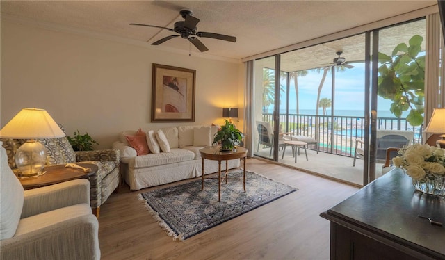 living room with ceiling fan, a water view, a textured ceiling, hardwood / wood-style floors, and floor to ceiling windows