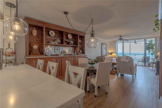 dining space featuring wood-type flooring, ceiling fan, a water view, and a wall of windows