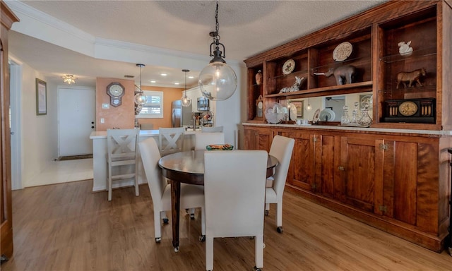 dining room featuring ornamental molding, light wood-type flooring, and a textured ceiling