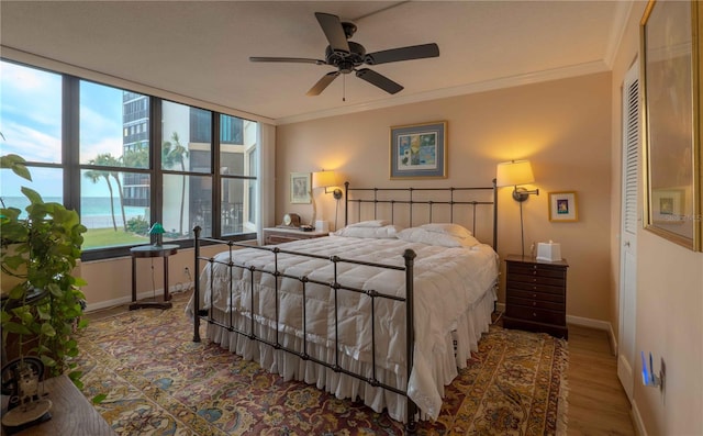 bedroom with a closet, crown molding, hardwood / wood-style floors, a water view, and ceiling fan