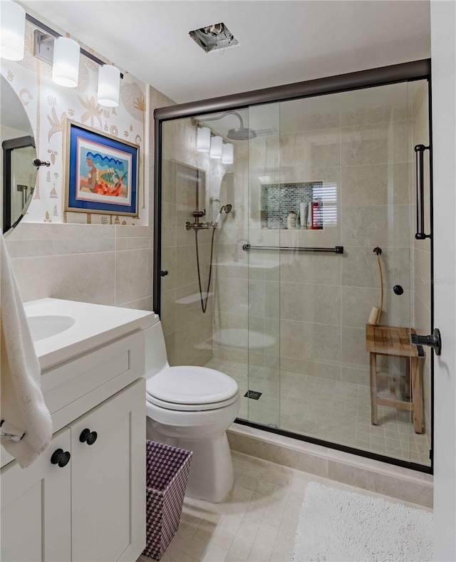 bathroom with a shower with door, tile floors, tile walls, vanity, and toilet