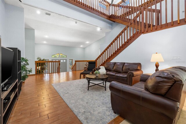 living room featuring rail lighting, light hardwood / wood-style floors, and a high ceiling