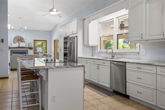 kitchen with appliances with stainless steel finishes, vaulted ceiling, ceiling fan, white cabinets, and a center island