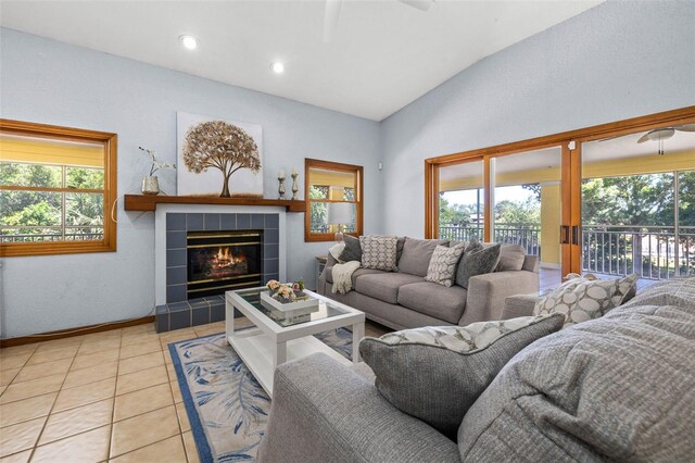 tiled living room with ceiling fan, a wealth of natural light, vaulted ceiling, and a tile fireplace