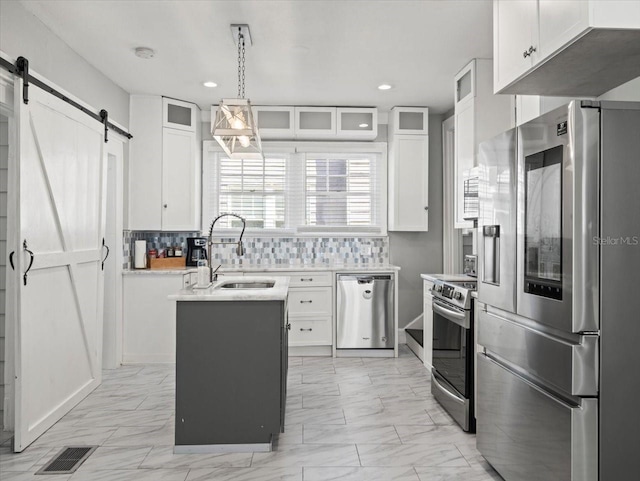 kitchen featuring a barn door, tasteful backsplash, white cabinetry, hanging light fixtures, and stainless steel appliances