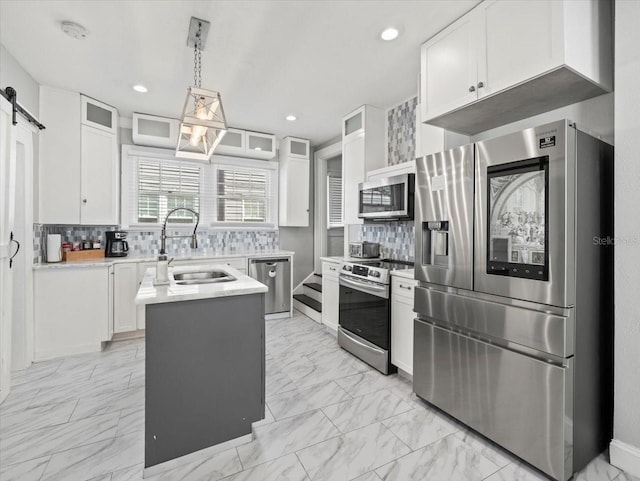 kitchen with white cabinetry, backsplash, appliances with stainless steel finishes, a barn door, and sink