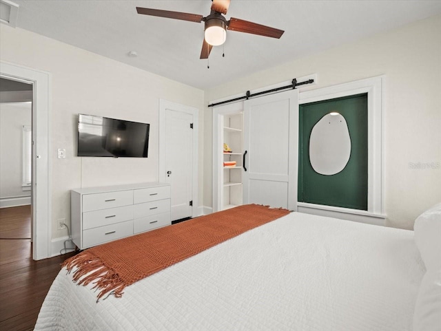 bedroom with a barn door, ceiling fan, and dark hardwood / wood-style floors