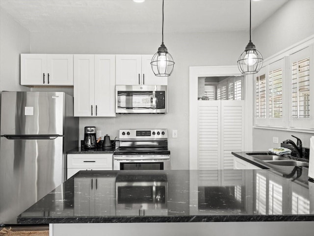 kitchen featuring decorative light fixtures, white cabinetry, appliances with stainless steel finishes, sink, and dark stone countertops