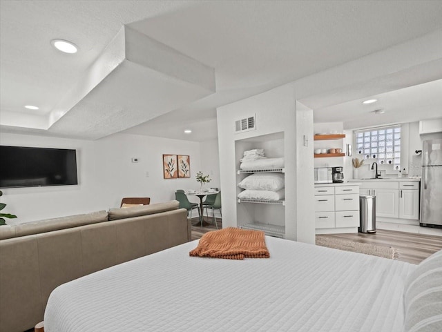 bedroom with light hardwood / wood-style flooring, sink, and stainless steel refrigerator