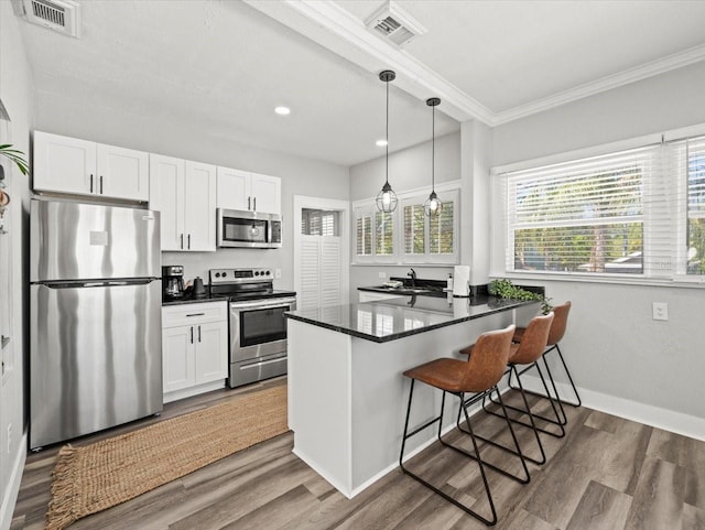 kitchen with kitchen peninsula, appliances with stainless steel finishes, wood-type flooring, and white cabinets