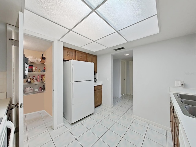 kitchen with a paneled ceiling, white appliances, sink, and light tile patterned floors