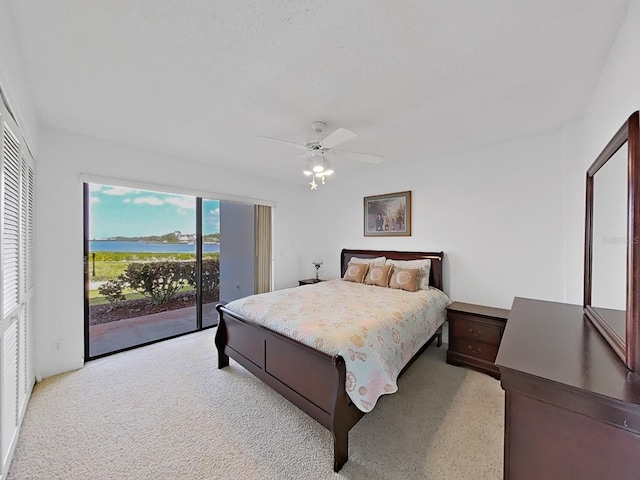 carpeted bedroom featuring ceiling fan, access to exterior, a water view, and a closet