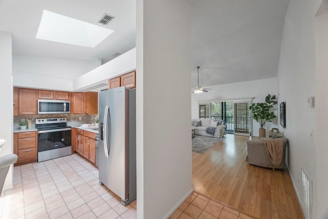 kitchen featuring appliances with stainless steel finishes, a skylight, tasteful backsplash, light wood-type flooring, and ceiling fan