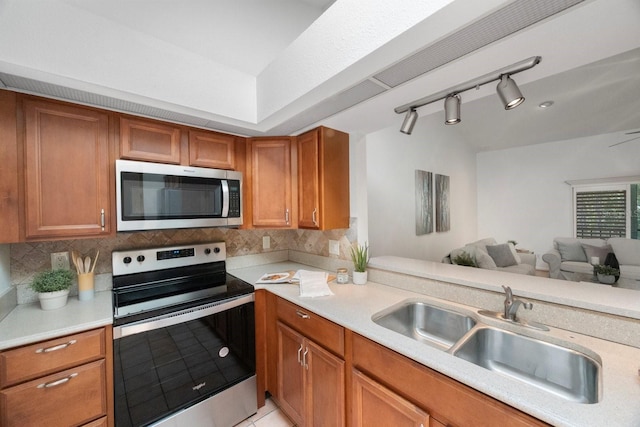 kitchen with backsplash, sink, rail lighting, stainless steel appliances, and kitchen peninsula