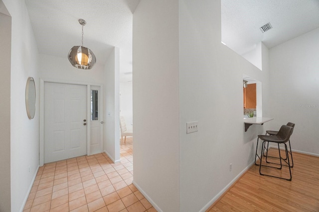 entryway featuring a textured ceiling, light tile patterned floors, visible vents, and baseboards