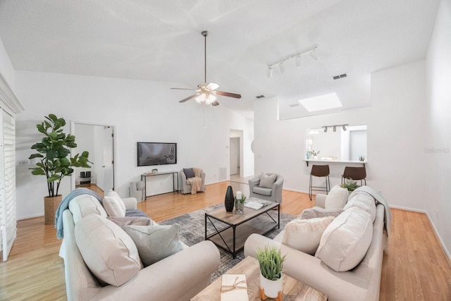 living room with ceiling fan, rail lighting, light wood-type flooring, and lofted ceiling with skylight