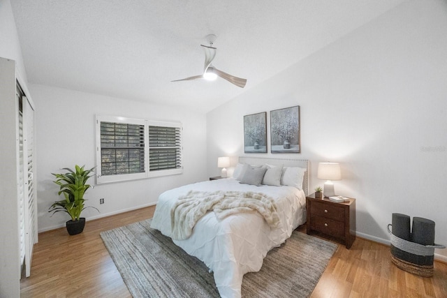 bedroom featuring light wood finished floors, ceiling fan, baseboards, and vaulted ceiling