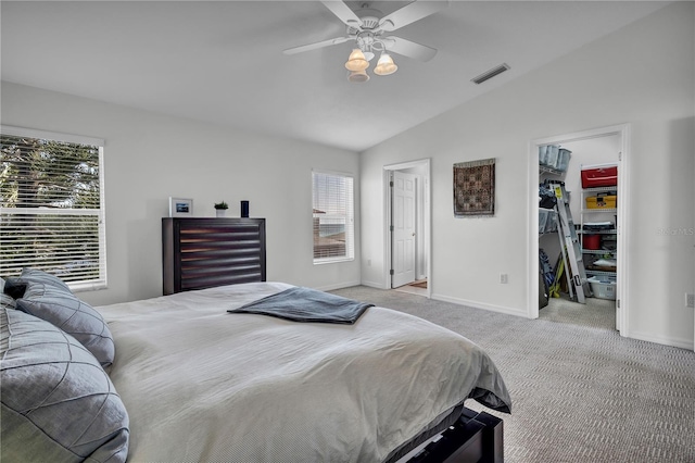 carpeted bedroom with multiple windows, a walk in closet, vaulted ceiling, and ceiling fan