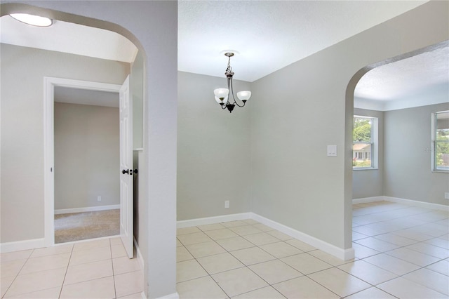 tiled spare room with a notable chandelier