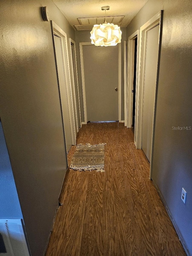 corridor with dark wood-type flooring and a notable chandelier