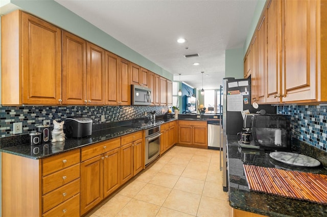 kitchen featuring stainless steel appliances, light tile flooring, tasteful backsplash, dark stone counters, and pendant lighting