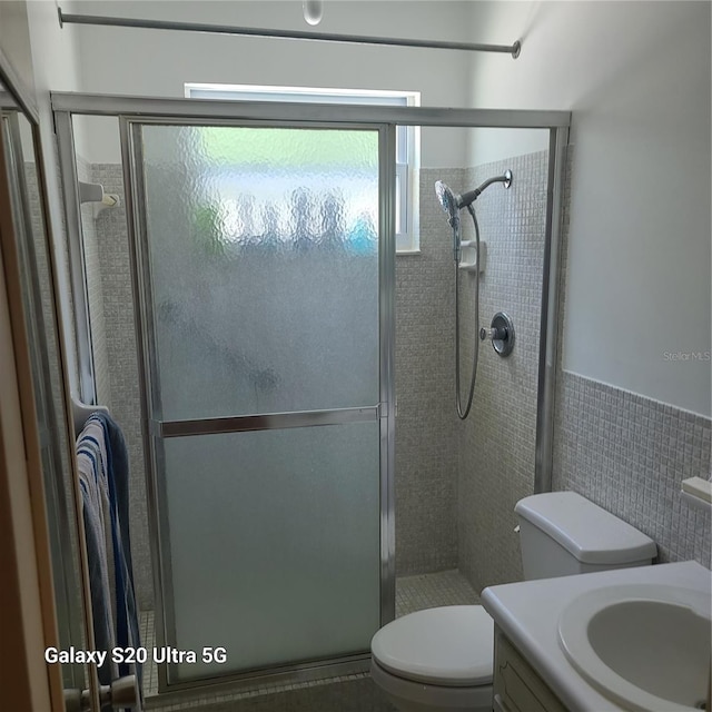 bathroom with tile walls, a shower with door, vanity, and toilet