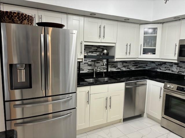 kitchen with appliances with stainless steel finishes, sink, backsplash, and white cabinetry