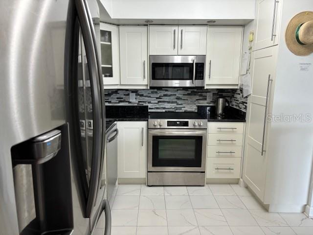 kitchen with appliances with stainless steel finishes, tasteful backsplash, light tile floors, and white cabinetry