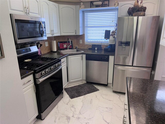 kitchen with white cabinetry, backsplash, stainless steel appliances, dark stone counters, and sink